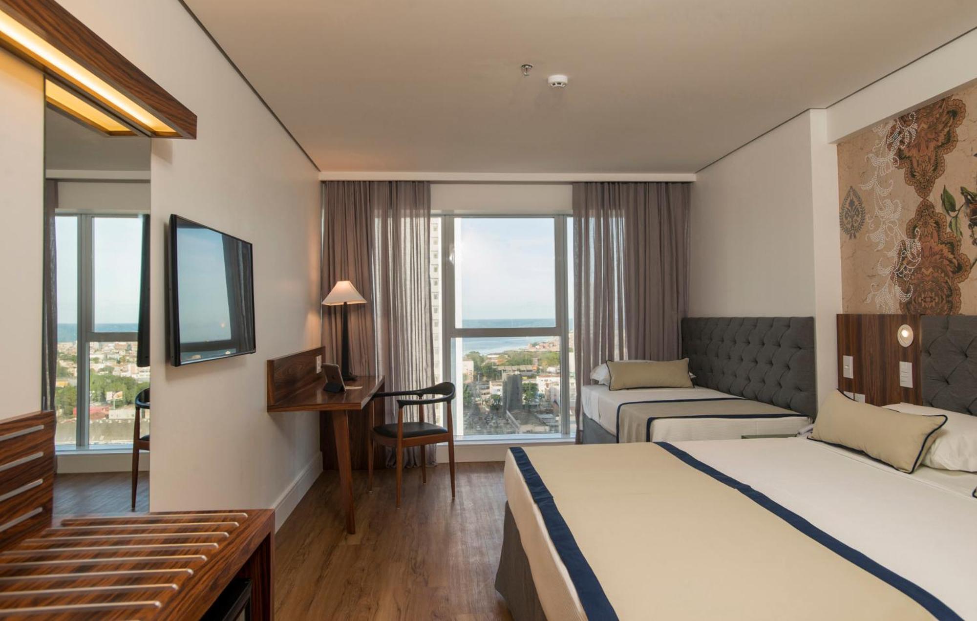 Hotel Luzeiros 헤시피 외부 사진 The photo shows a hotel room that features a modern and comfortable design. There are two beds: one larger bed and a smaller twin bed. The room has large windows with curtains that allow natural light to enter, offering a view of the outside, possibl